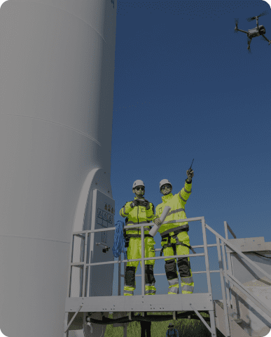 Workers inspecting wind turbine with drone.