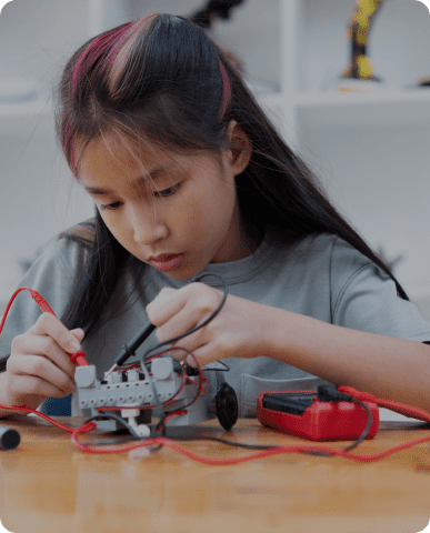 Girl building robot with wires and tools.