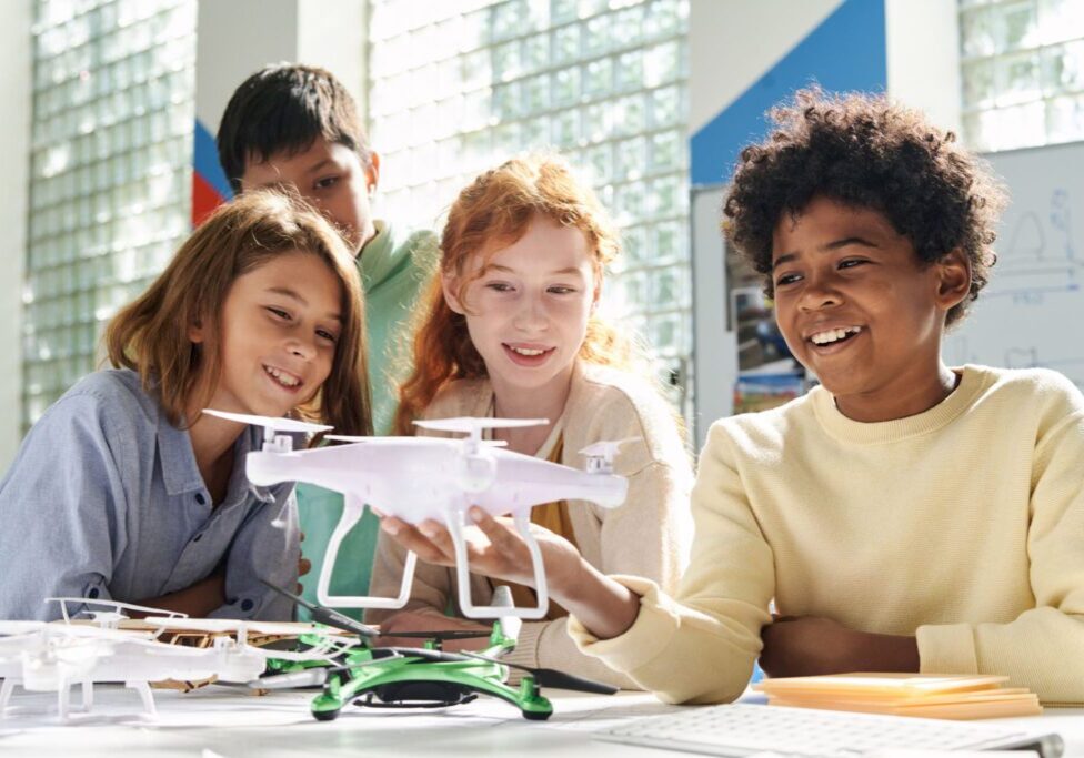 Kids smiling and holding a drone indoors.